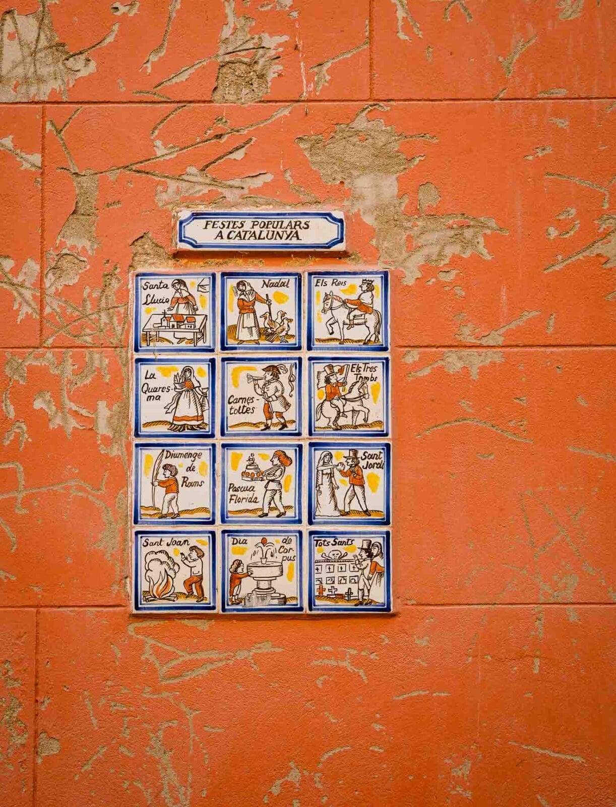 Straßenschild aus Kacheln an einer orangefarbenen Hauswand in der Barceloneta