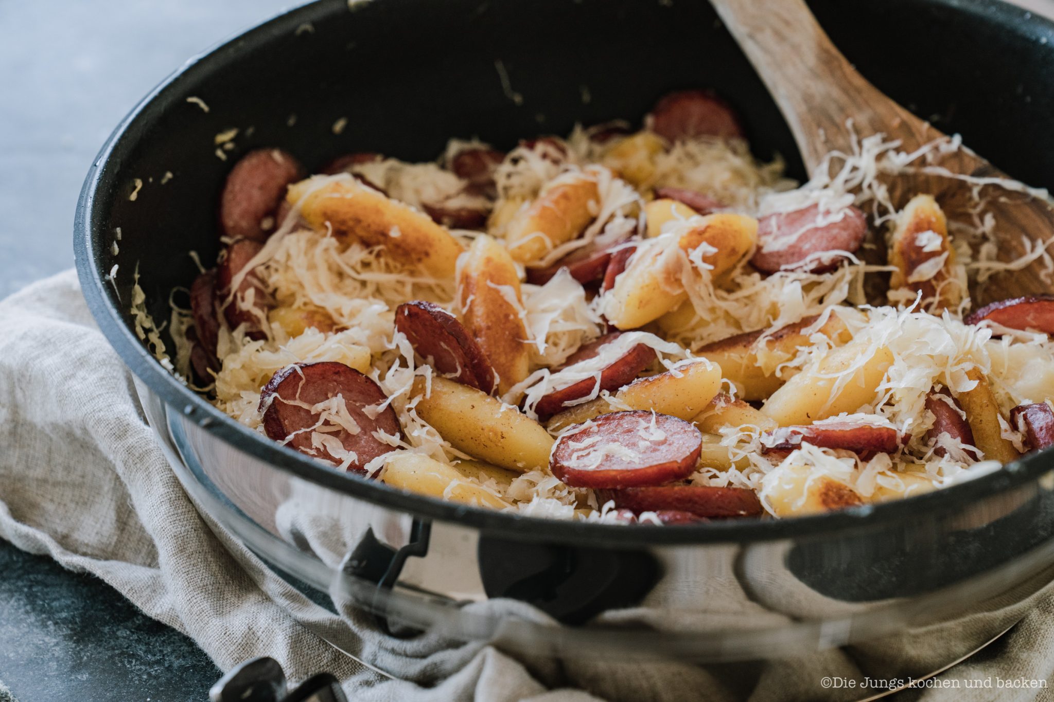 Tefal Pfannengerichte 17 scaled | Schupfnudeln mit Kraut und Kabanossi. Zum einen ist das ein Gericht, das Sascha's Mama früher oft zubereitet und das die Familie immer gerne gegessen hat. Zum anderen verarbeitet Torsten's Mama jedes Jahr mit ihrer Freundin Brigitte Weißkohl zu Sauerkraut. Das Kraut wird in einem alten kühlen Keller in Steingut-Behältern gelagert und zum Jahresbeginn ist es fertig. Meist wird ein Teil dann noch schnell während der kalten Jahreszeit verputzt, aber ein großer Teil wird zum Einfrieren an die Familie verteilt. Also haben wir endlich das Rezept für Krautschupfnudeln mit Kabanossi aufgeschrieben.