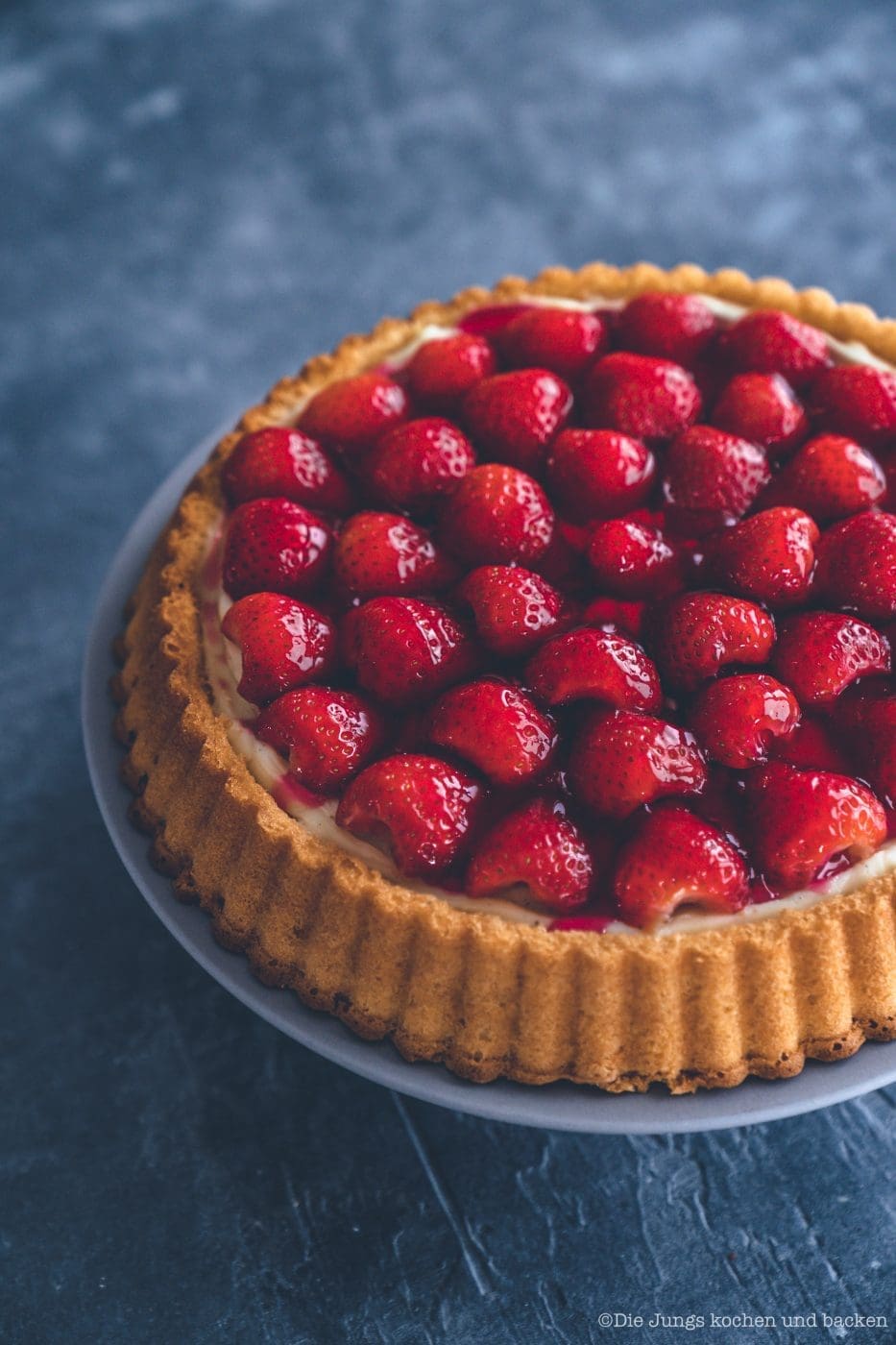 Erdbeerkuchen mit Pudding 3 | Heute kommen wir wieder mit einem schnellen Klassiker von zu Hause. Eine ganz klassischee Erdbeerkuchen mit Pudding. Ein simpler Obstboden mit etwas Puddingcreme und frischen Erdbeeren drauf. Das ist auch wieder so etwas, dass Oma Lore früher immer schnell mal so aus dem Nichts gezaubert hat. Immer dann, wenn entweder unangekündigter Besuch vor der Türe stand oder sie die Erdbeeren aus dem Garten verarbeiten wollte, damit sie sich nicht zu lange im Kühlschrank stapelten.