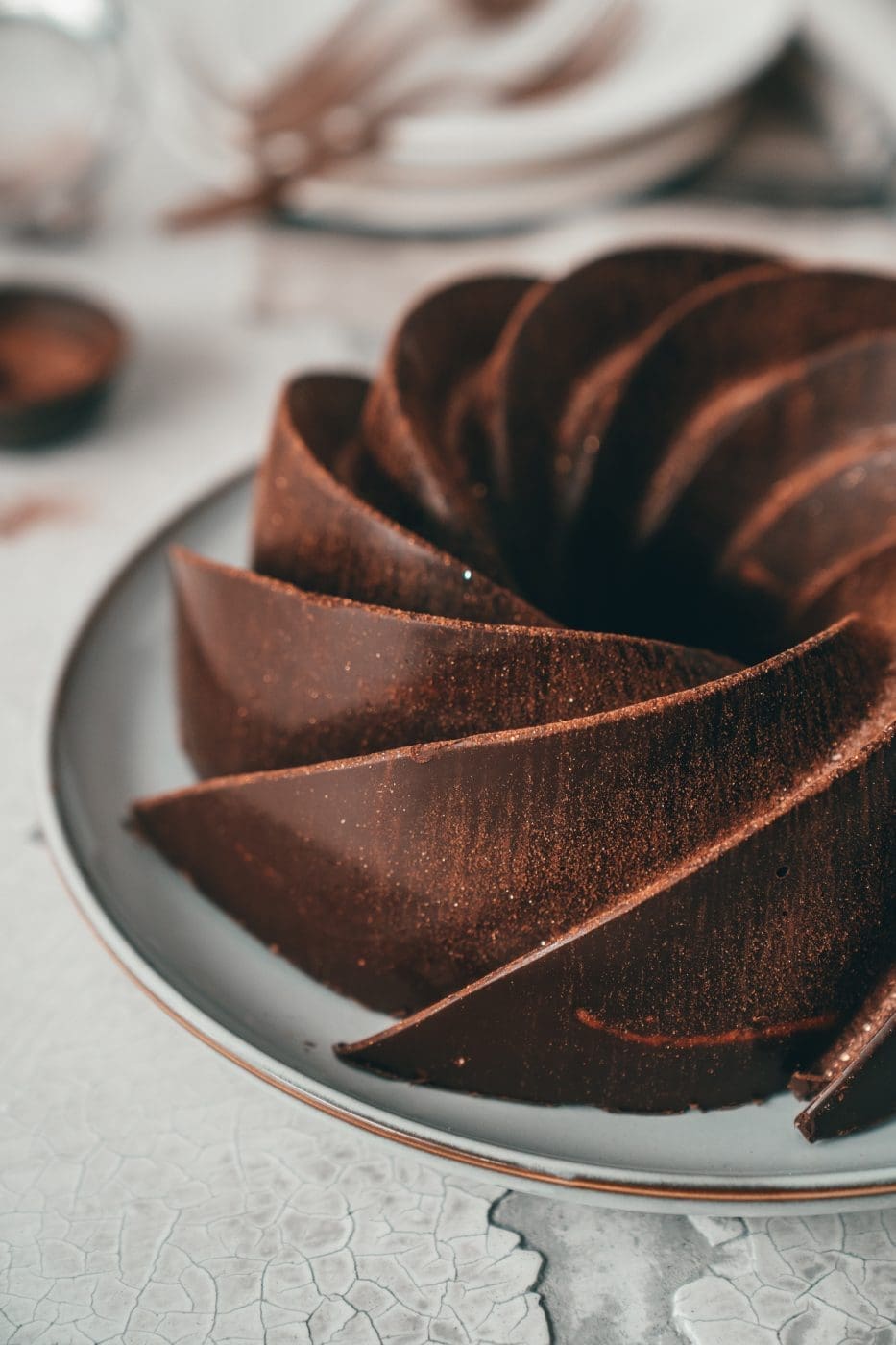Zimt-Marmorkuchen mit glänzender Schokoglasur auf einer hellen Platte, dahinter Teller und Kuchengabeln
