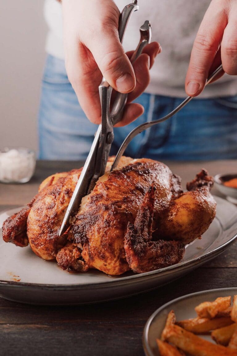 Knuspriges Brathähnchen wird mit der Geflügelschere tranchiert, dazu Pommes