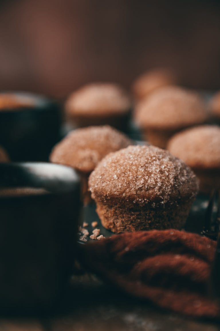 Zimt-Zucker-Muffin mit Zimtzucker-Kruste vor weiteren Muffins und einer Tasse Kaffee