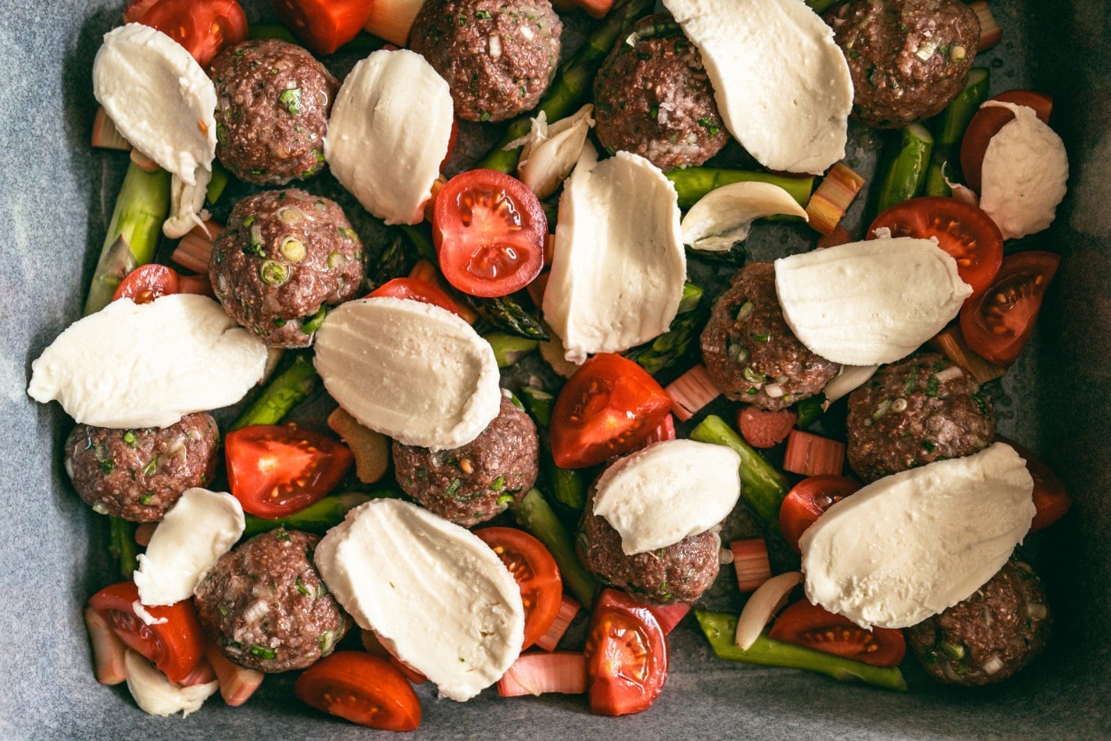 Bestückte Auflaufform mit Hackbällchen, grünem Spargel und Rhabarber vor dem Backen