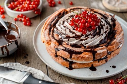 Churros-Torte mit Zimtcreme, Schokosauce und roten Johannisbeeren auf einer Tortenplatte