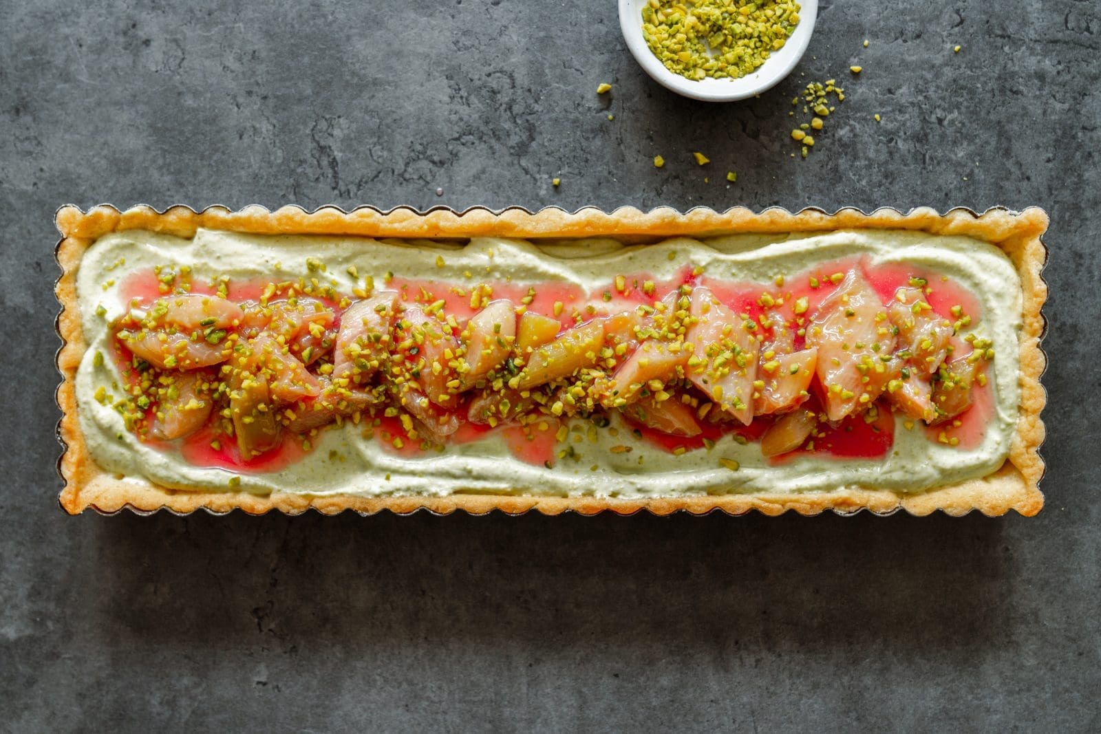 Pistazien-Tarte mit Rhabarber | Unser Frühlingskuchen mit Vermouth 1 Pistazien-Tarte mit Rhabarber quer im Bild mit gemahlenen Pistazien im Hintergrund