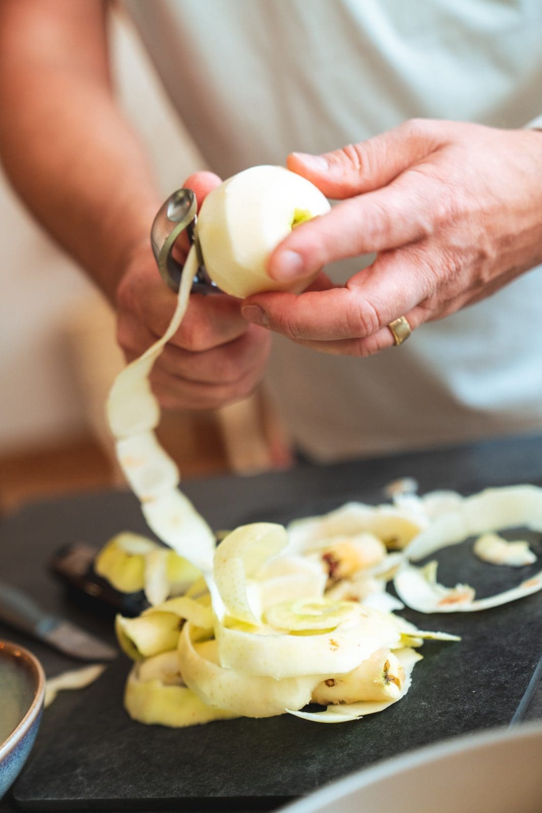 Ein Apfel wird mit dem Sparschäler geschält, die Schale liegt daneben