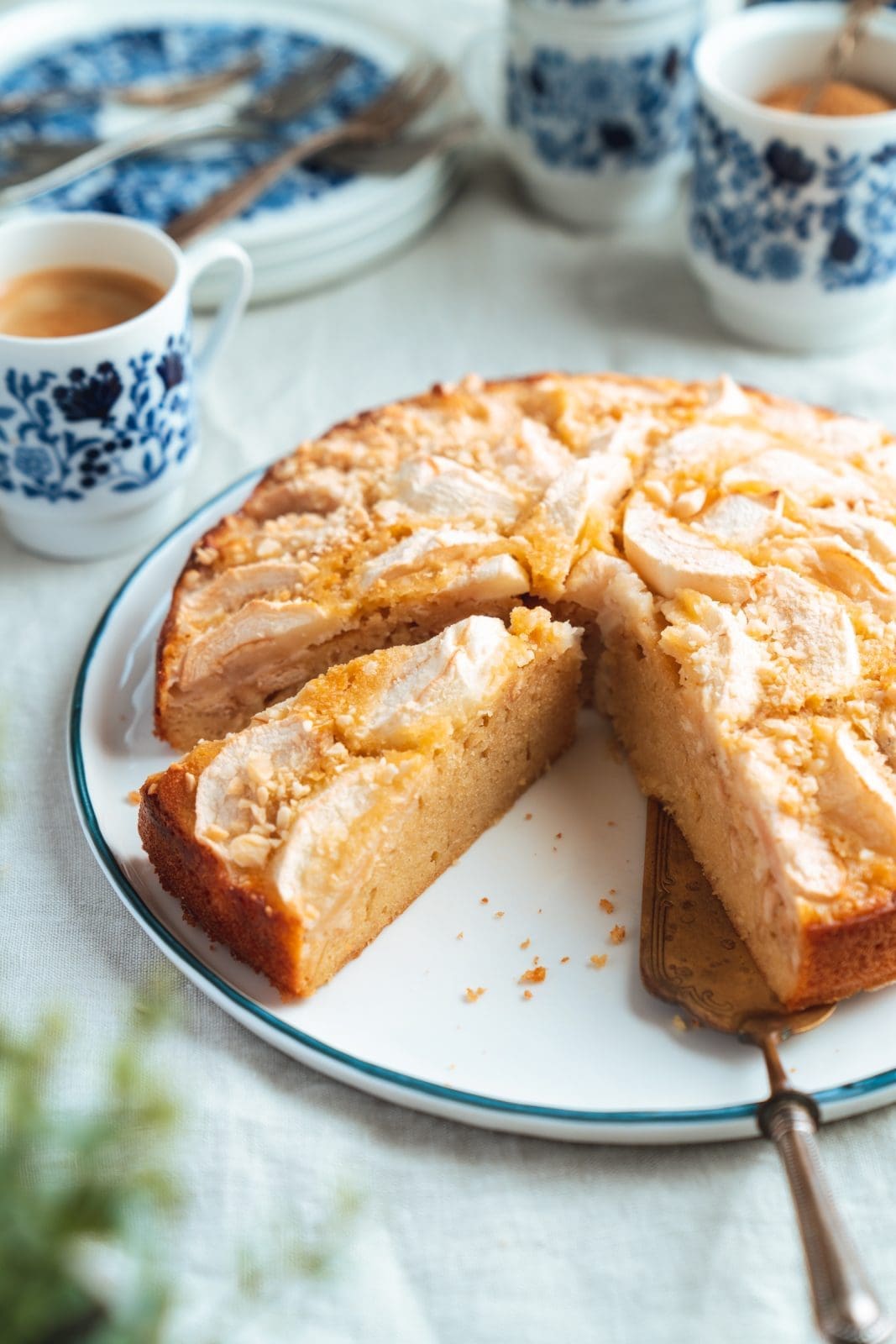 Angeschnittene Appeltaart auf einer Kuchenplatte neben blau gemustertem Kaffeegeschirr