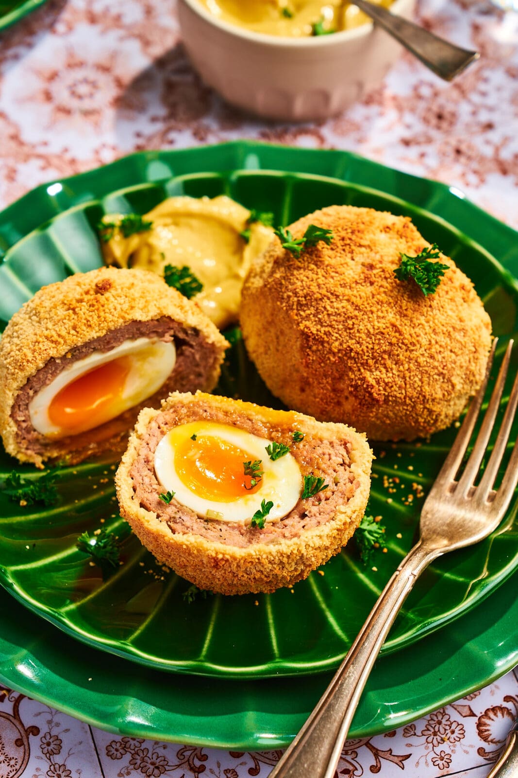 Halbiertes Scotch Egg auf einem grünen Teller mit flüssigem Eigelb und knuspriger Panade, serviert mit Senf.