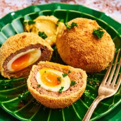 Halbiertes Scotch Egg auf einem grünen Teller mit flüssigem Eigelb und knuspriger Panade, serviert mit Senf.
