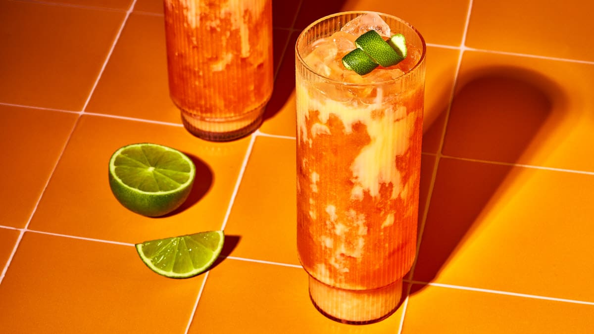 Der ultimative Oster-Cocktail serviert in hohen Rillengläsern auf modernen warm-orangen Kacheln.