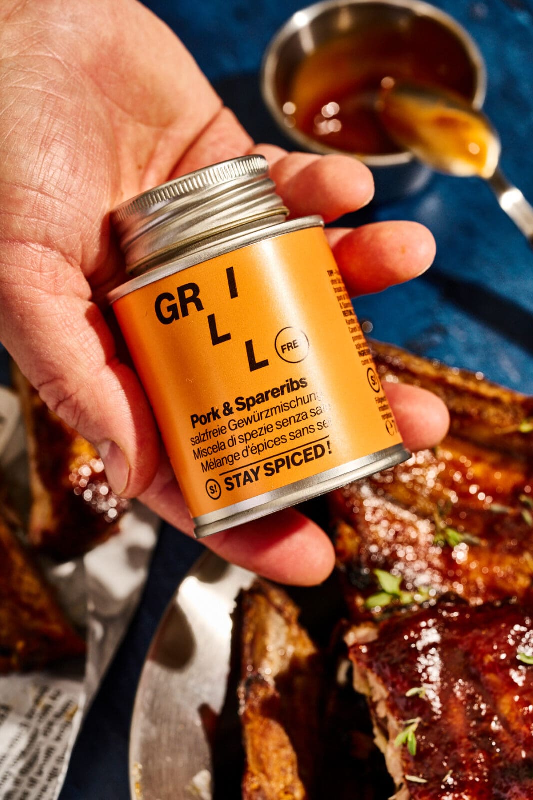Hand hält eine Dose STAY SPICED ! Grillgewürz Pork und Spareribs über glasierten Spareribs