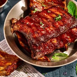 Fertig gebackene Spareribs auf einem Teller mit Glasur im Hintergrund