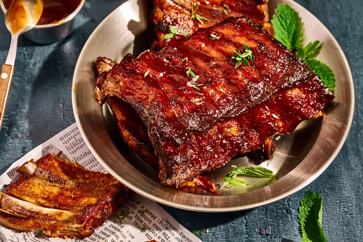 Fertig gebackene Spareribs auf einem Teller mit Glasur im Hintergrund