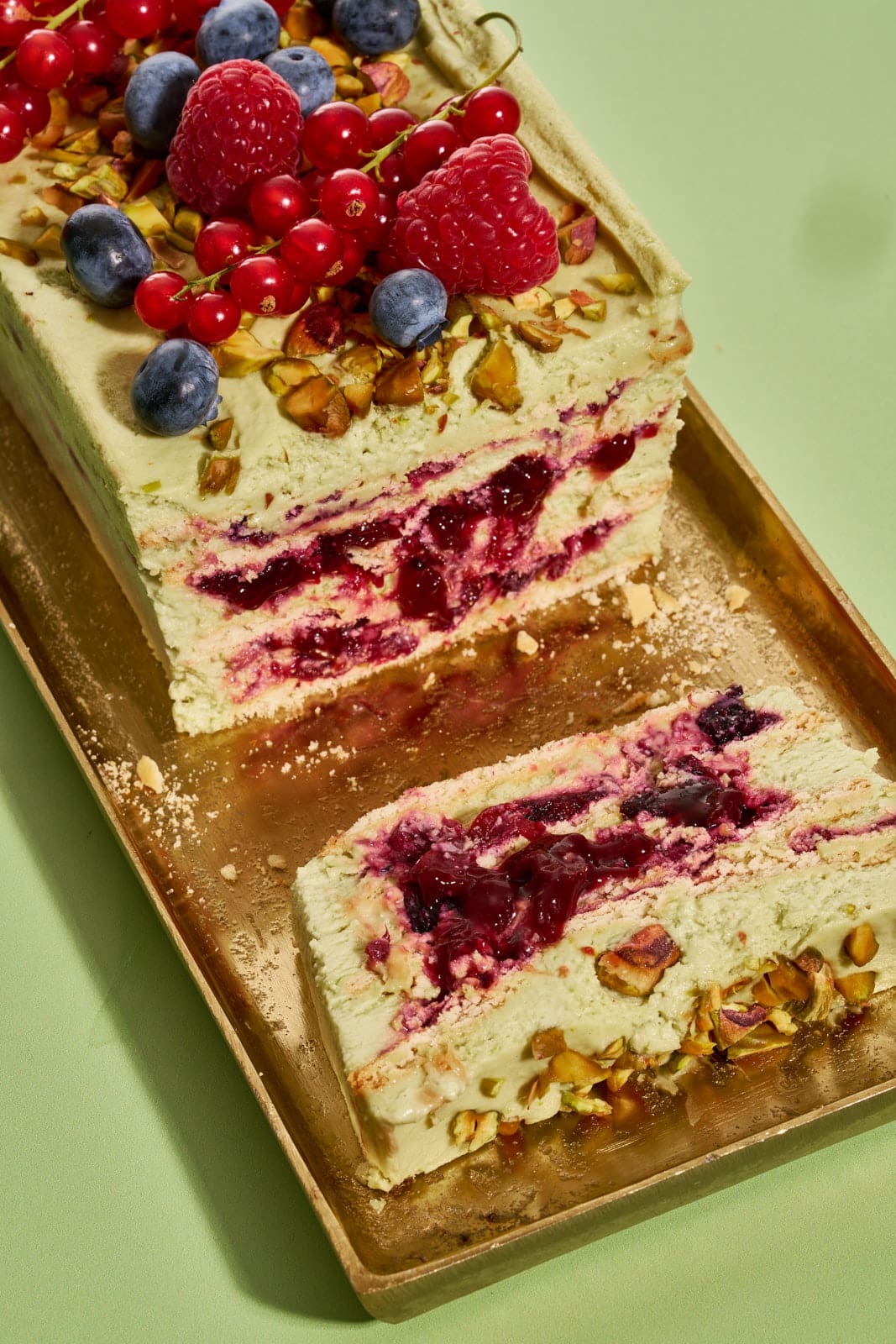 Cremiger Pistazienkuchen ohne Backen von der Seite, Schichten aus Pistaziencreme und Waldbeeren-Kompott sichtbar