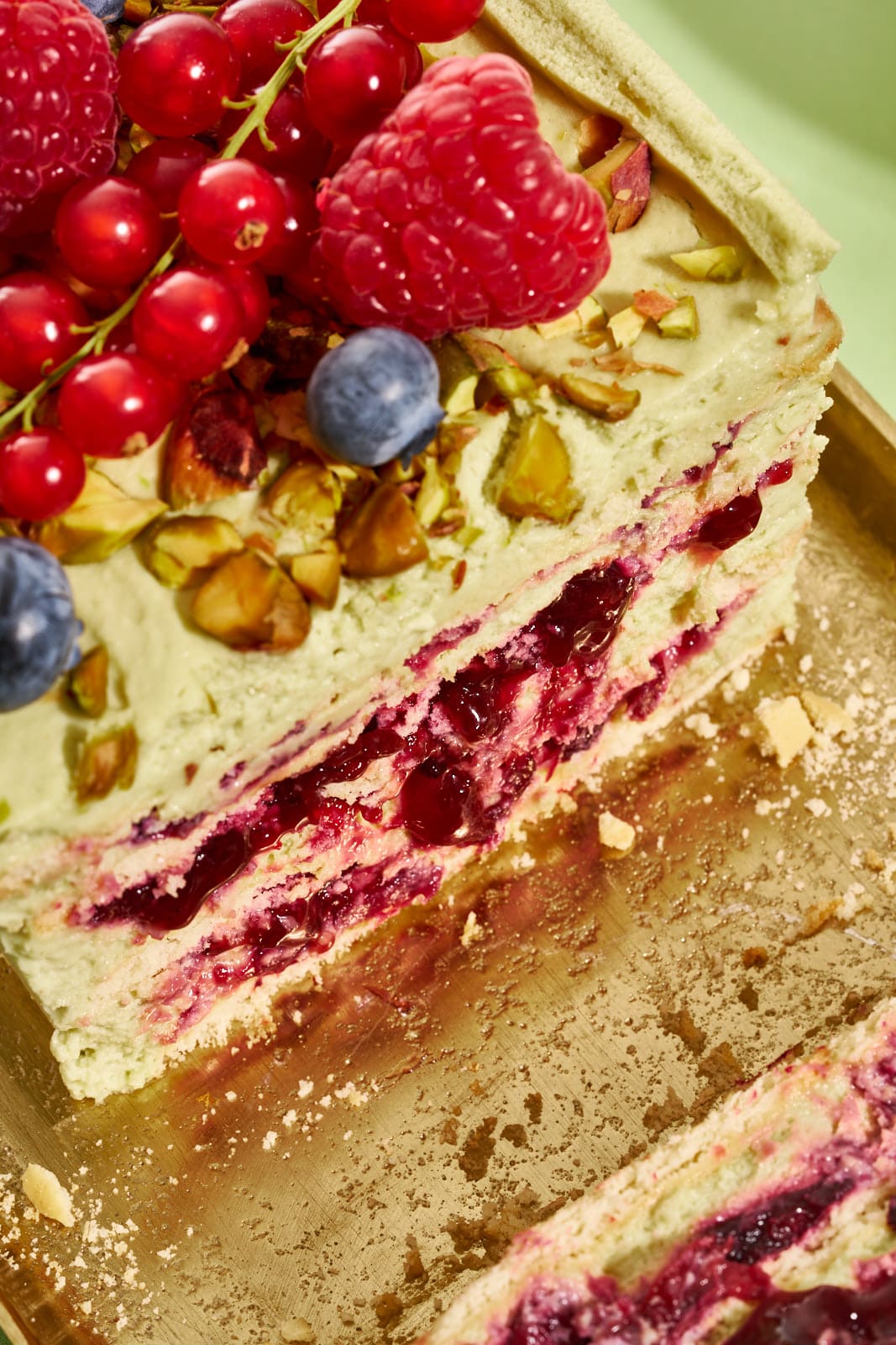 Nahaufnahme der Schichten aus Waldbeeren-Kompott, Pistaziencreme und weichen Butterkeksen im No-Bake-Kuchen
