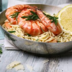 Pasta mit Garnelen in Gin-Zitronen-Sauce in einer Edelstahlpfanne, garniert mit Rosmarin, Pfeffer und einer Zitronenscheibe