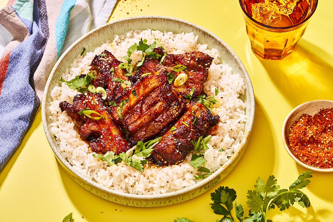 Teller mit koreanischem Schweinebauch, Reis, Koriander und Frühlingszwiebeln auf gelbem Untergrund