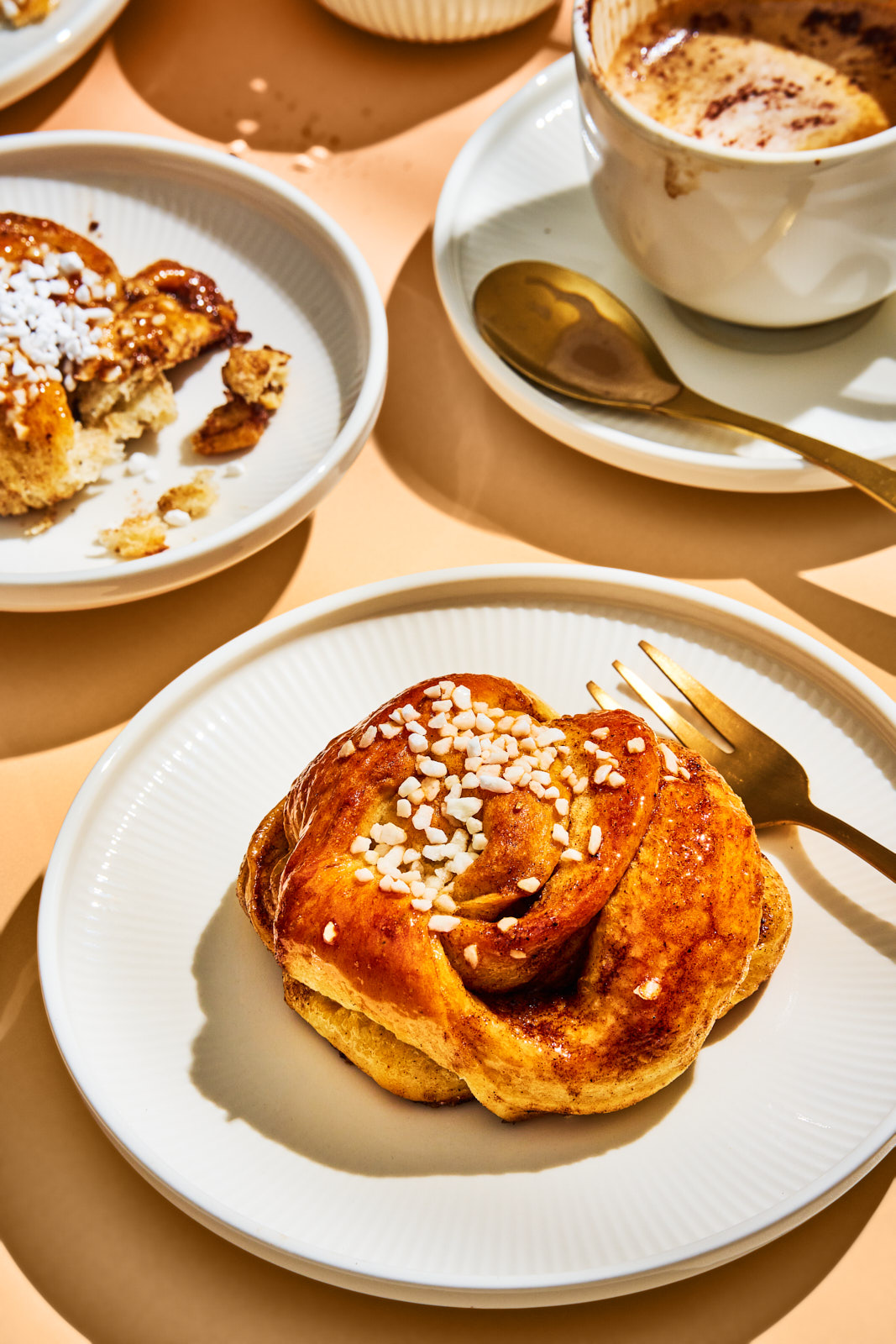 Kanelsnurrer. Dänische Zimtknoten mit Kardamom 2 Gebackene Kanelsnurrer mit Hagelzucker auf Tellern, dazu eine Tasse Kaffee