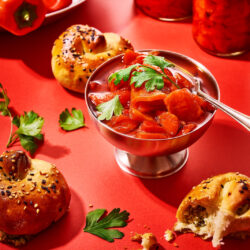 Eingelegte Paprika. Mediterrane Antipasti aus dem Airfryer 30 Eingelegte Paprika in einer silbernen Schale mit frischen Kräutern, daneben Sesambrötchen und Gläser mit Antipasti