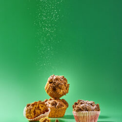 Gestapelte Kürbis-Muffins mit Streuseln, ein Muffin aufgebrochen, Puderzucker rieselt von oben
