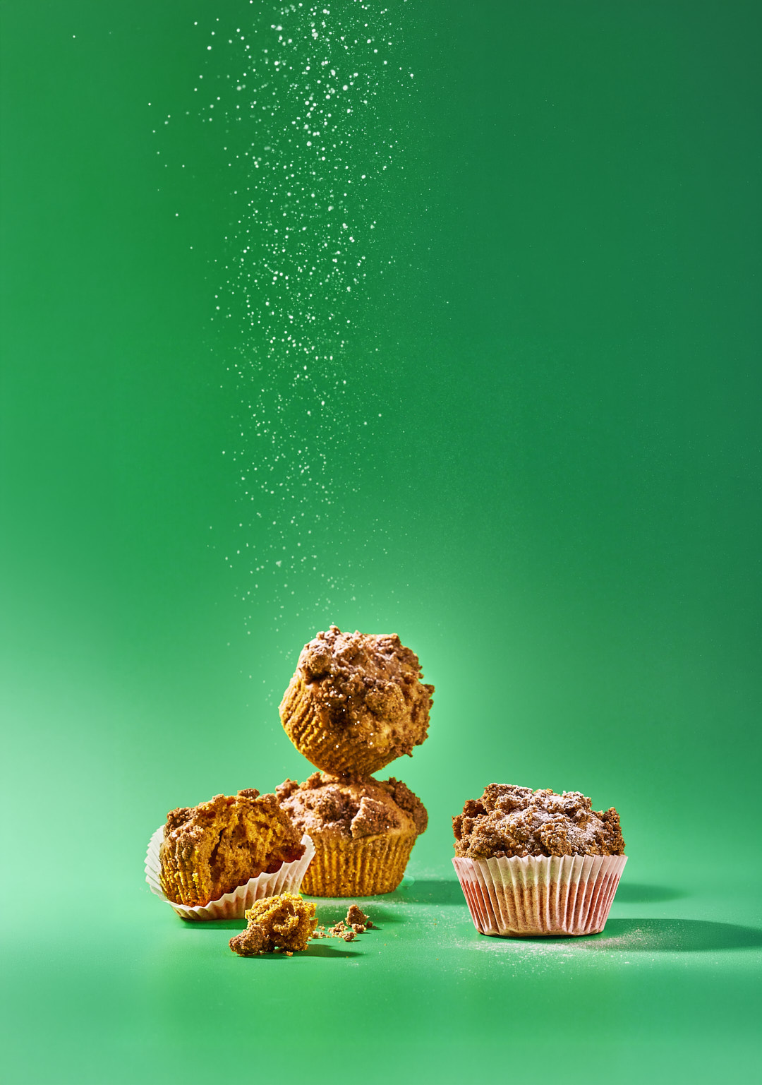 Pumpkin Spice Rezepte aus dem Adventskalender. Latte, Porridge und Kürbis-Muffins 8 Gestapelte Kürbis-Muffins mit Streuseln, ein Muffin aufgebrochen, Puderzucker rieselt von oben