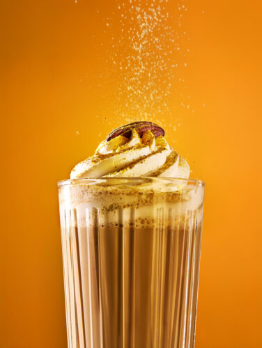 Pumpkin Spice Latte im Glas mit Sahnehaube und Pekannuss, bestäubt mit Pumpkin Spice Latte Gewürz